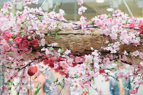 Decorative wicker basket with pink flowers is suspended from the ceiling by iron chains. The concept of floral, botanical and interior design decorations. Close up shot photo