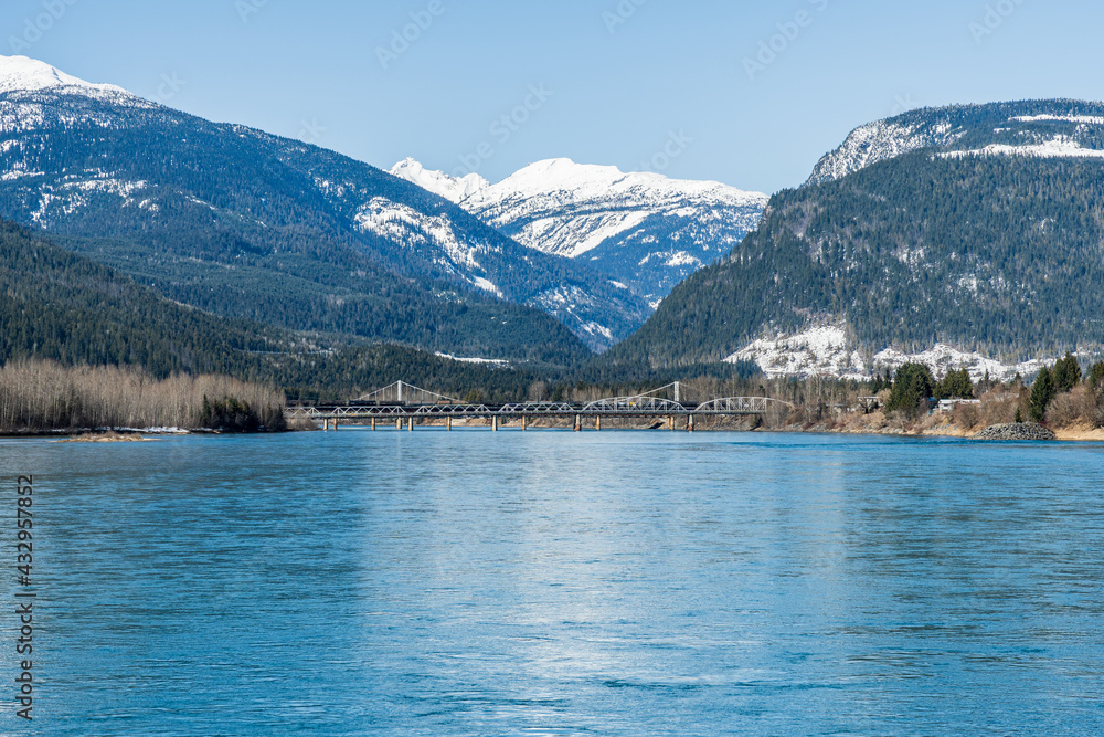 Bridge over Columbia river with snow on mountains blue sky early spring British Columbia Canada.