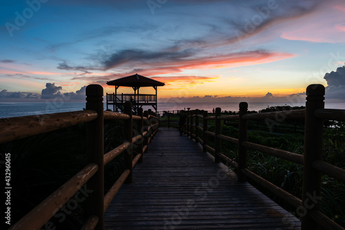 Wooden path that leads to a lookout to contemplate the beautiful sunset with colorful clouds. Person standing in the darkness looking at the phone and another looking at the sunset.