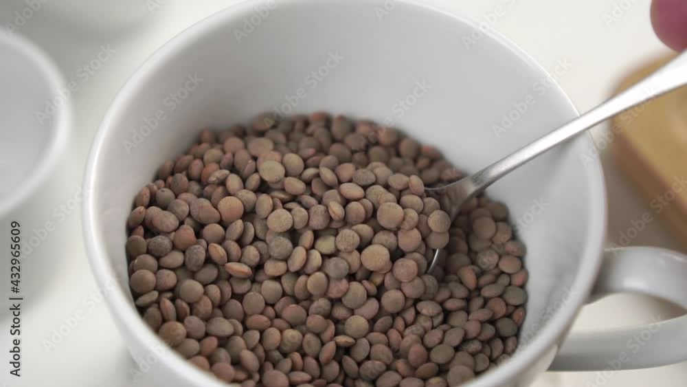 Stirring raw lentils with a spoon in a white cup on the kitchen table close-up. Slow motion. Cooking traditional meals Stirring raw lentils with a spoon in a white cup on the kitchen table close-up. Slow motion. Cooking traditional meals