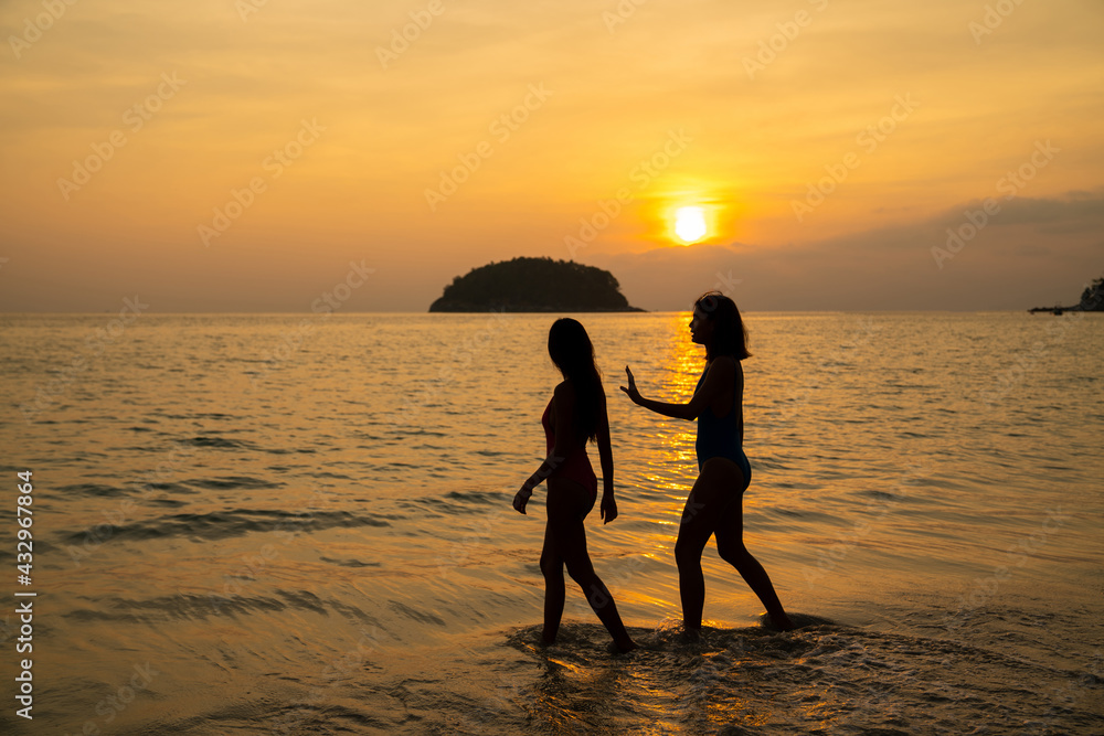 Obraz premium Asian woman friendship in colorful swimwear walking and playing sea water together on the beach at summer sunset. Female girl friends enjoy and having fun outdoor activity lifestyle on summer vacation