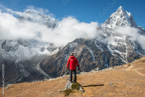 Man in red sweater standing in front of Mt.Taboche (6,501 m) and Mt.Cholatse (6,440 m) during trekking from Lobuche to Dzongla village in Nepal. Conceptual shot of traveling in Himalayas. photo