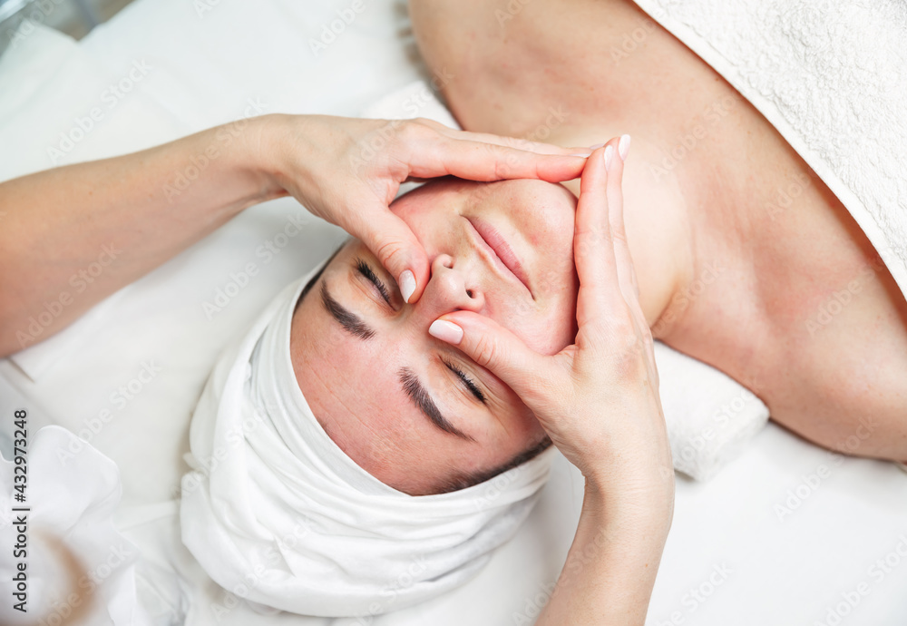 Beautiful girl has a facial massage in a beauty clinic. Cosmetologist doing massage for woman. Facial massage beauty treatment. Young woman lying with closed eyes and having face and head massage Beautiful girl has a facial massage in a beauty clinic. Cosmetologist doing massage for woman. Facial massage beauty treatment. Young woman lying with closed eyes and having face and head massage