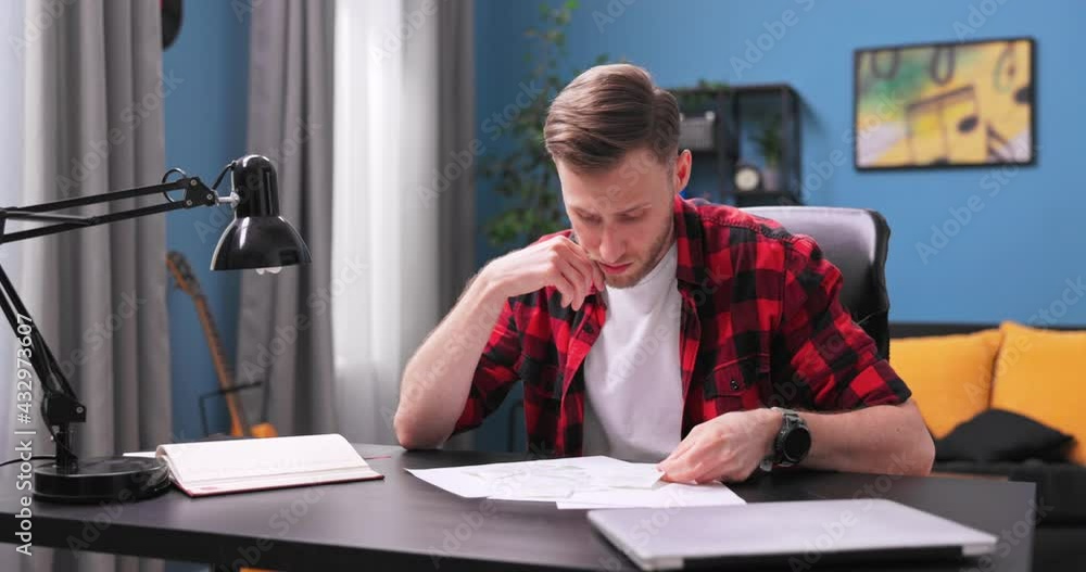 A tired young man sits at his desk in his room and reviews his apartment bills. The young boy analyzes the cost of living and worries about the future. A tired young man sits at his desk in his room and reviews his apartment bills. The young boy analyzes the cost of living and worries about the future.