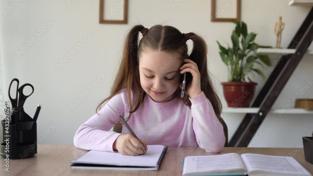 The teacher dictates homework by phone, the student writes notes in a workbook while sitting at the table, studying distance online. Education concept with gadgets and mobile network. The teacher dictates homework by phone, the student writes notes in a workbook while sitting at the table, studying distance online. Education concept with gadgets and mobile network.