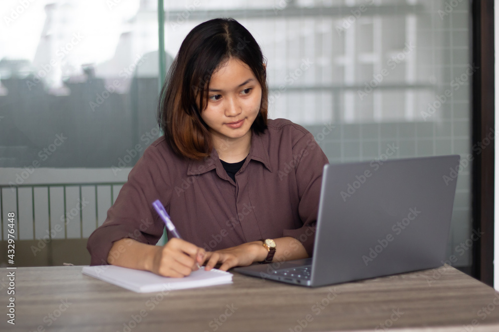 Young asian woman sitting at table doing assignments in college library. Young asian woman sitting at table doing assignments in college library.