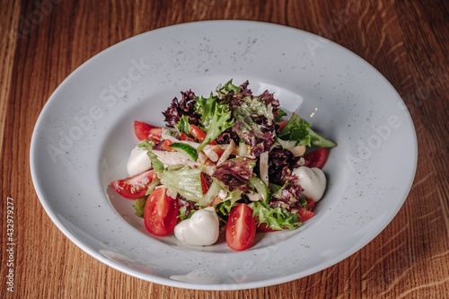 White plate with salad stands on a wooden table in a restaurant. Appetizing light salad with herbs, lime, tomatoes and cabbage.
