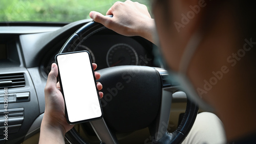 Close up view businessman wearing protective mask and using mobile phone while driving car.