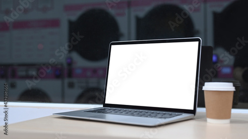 Laptop computer and cup of coffee on white table with row of washing machines in background.