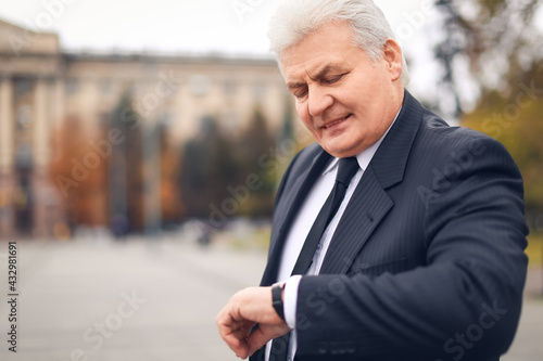 Senior businessman looking at wristwatch outdoors
