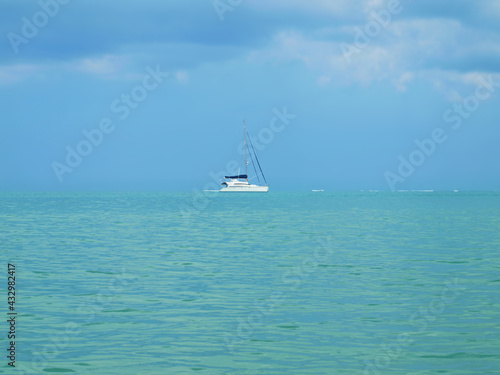 Blue calm sea, sky with beautiful clouds, white sailing yacht on a horizon. Panoramic view. Yachting in the ocean. Turquoise water, no wind. Cruise, summer traveling, tour tourism. Must without sail. 