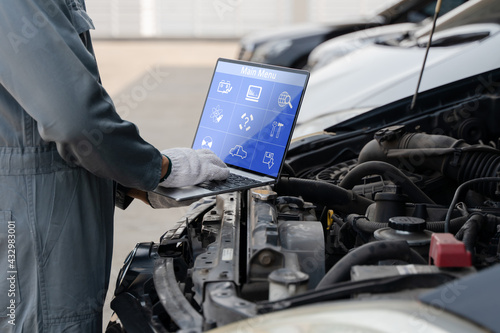 Mechanic using a laptop computer to check collect information during work a car engine. service maintenance of industrial to engine repair.