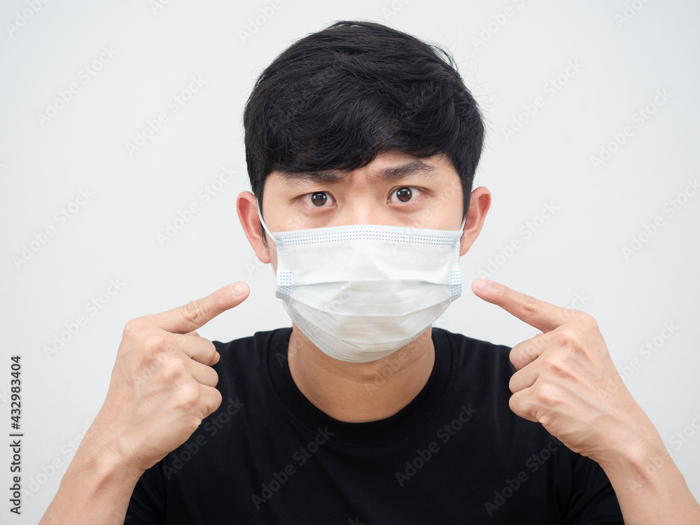 Closeup face of man serious point finger at protect mask at his face against covid-19 concept on white background Closeup face of man serious point finger at protect mask at his face against covid-19 concept on white background