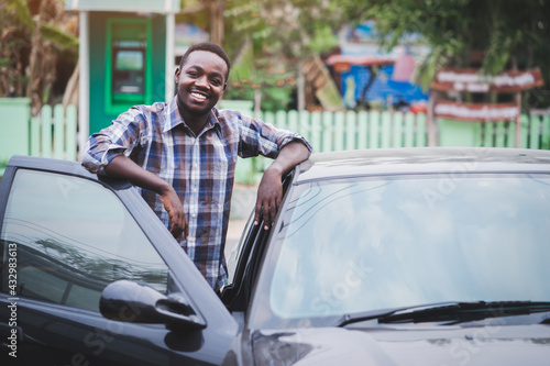 African man standing and smiling with a car in village