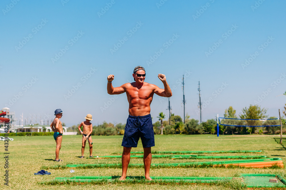 Tanned muscular man dances on the playground for minigolf in the summer