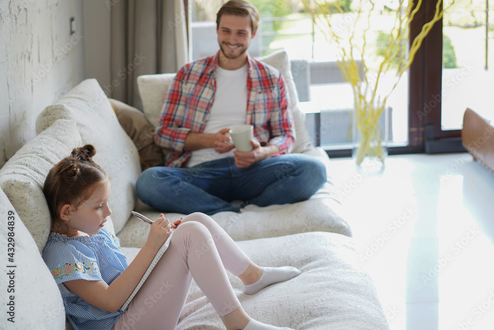 Happy father smilling daughter sitting on sofa enjoying creative activity, drawing pen pictures in albums, father and daughter spend free time together. Happy father smilling daughter sitting on sofa enjoying creative activity, drawing pen pictures in albums, father and daughter spend free time together.