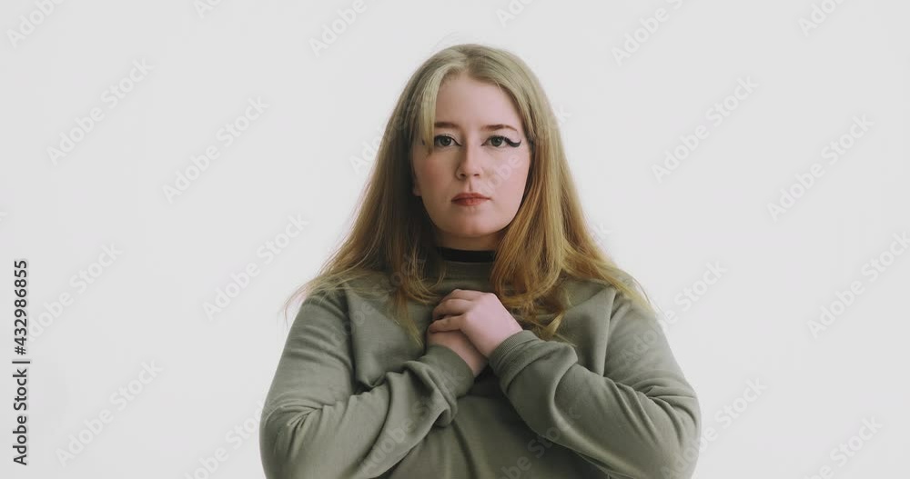Hopeful plump blonde woman in green sweatshirt puts hands to chest posing for camera at white wall at audition closeup slow motion Hopeful plump blonde woman in green sweatshirt puts hands to chest posing for camera at white wall at audition closeup slow motion