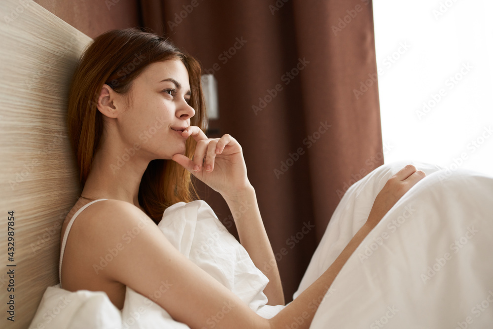 happy woman under the covers in bed near the window in the morning dreamy look model happy woman under the covers in bed near the window in the morning dreamy look model