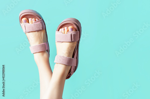 Female legs in pink sandals upside down on blue background.