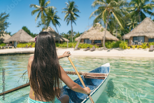 Outrigger Canoe woman paddling in traditional French Polynesian boat for recreational activity and watersport competition. Bora Bora overwater bungalow resort hotel sport exercise lifestyle.