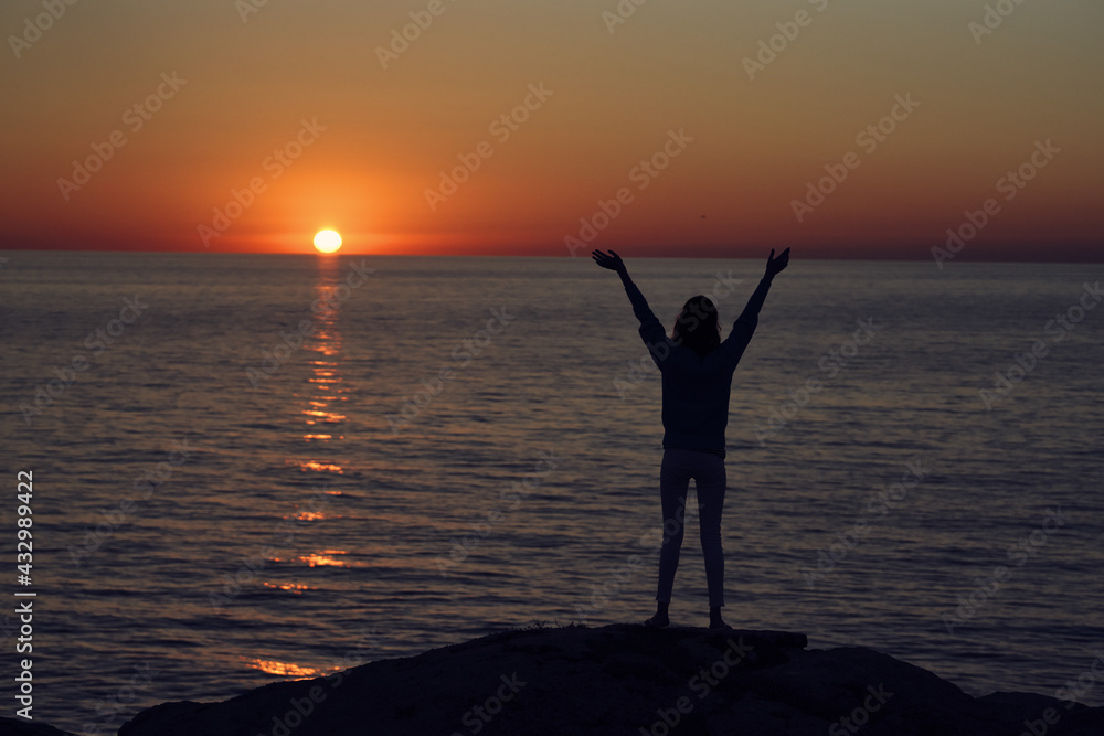 silhouette of a man with hands raised up on the beach and sunset in the background