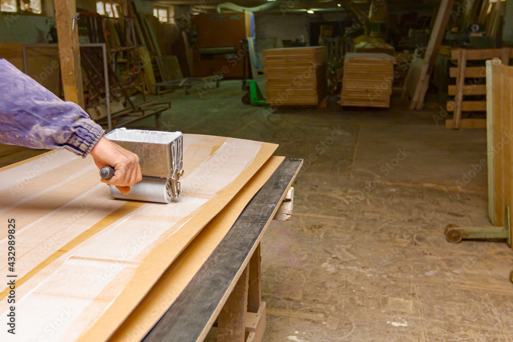 Carpenter smears the plywood with hand roller tool, spreader for evenly application of glue on the wooden surface Carpenter smears the plywood with hand roller tool, spreader for evenly application of glue on the wooden surface