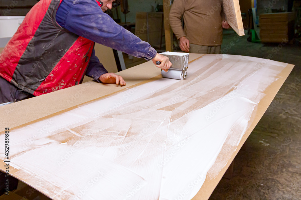 Ταπετσαρία Carpenter smears the plywood with hand roller tool, spreader for evenly applicat