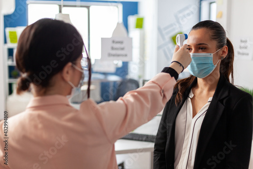 Woman using infrared thermometer measuring office worker temperature  during global epidemic with coronavirus in business company. New normal in time of world pandemic with covid19.