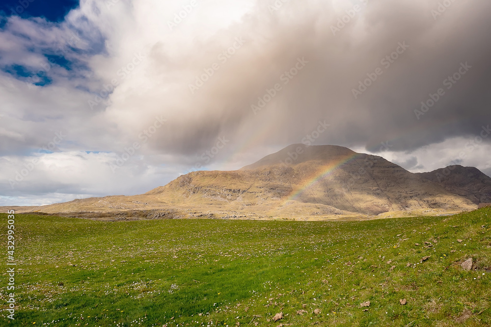 Rainbow in a mountains. Connemara, county Galway, Ireland. Green grass field in foreground, mountain in the background. Nobody. Irish landscape. Cloudy sky Rainbow in a mountains. Connemara, county Galway, Ireland. Green grass field in foreground, mountain in the background. Nobody. Irish landscape. Cloudy sky