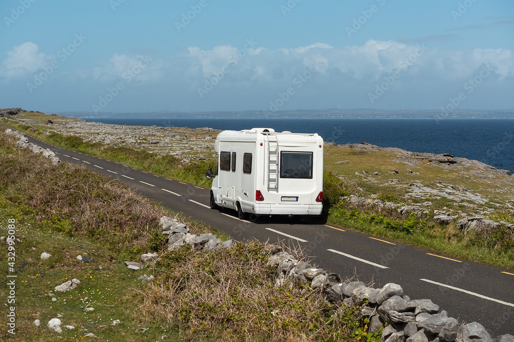 White camper van on a small asphalt road by the ocean. Traveling in motor home concept. Warm sunny day. Clear blue sky. Beautiful nature enviroment