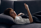 a woman lies on a gray sofa with a mobile phone in her hand