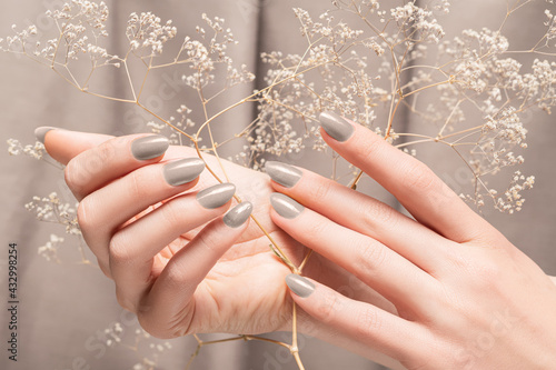 Female hands with glitter gray nail design. Female hands hold autumn flower. Woman hands on beige fabric background