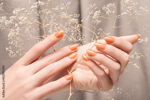 Female hands with glitter beige nail design. Female hands hold autumn flower. Woman hands on beige fabric background