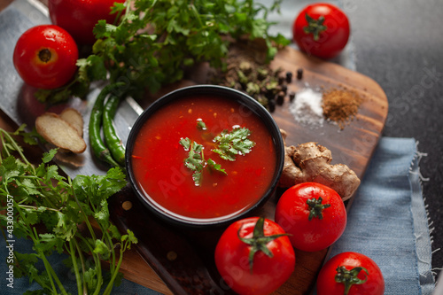 Close-up of Indian Homemade fresh and healthy tomato soup garnished with fresh coriander leaves and ingredients and herbs, served in a black bowl over the wooden top background. 