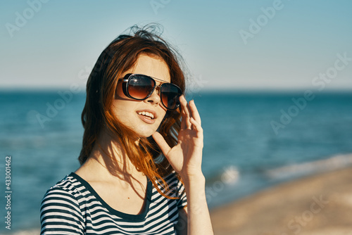 a woman in a t-shirt and glasses walks along the sandy shore on the beach near the blue sea