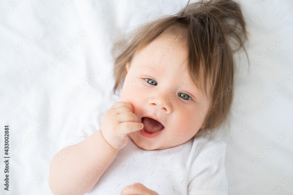 portrait of funny baby boy with finger in a mouth smiling and lying on a white bedding at home. portrait of funny baby boy with finger in a mouth smiling and lying on a white bedding at home.
