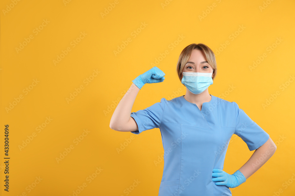 Doctor with protective mask showing muscles on yellow background, space for text. Strong immunity concept Doctor with protective mask showing muscles on yellow background, space for text. Strong immunity concept