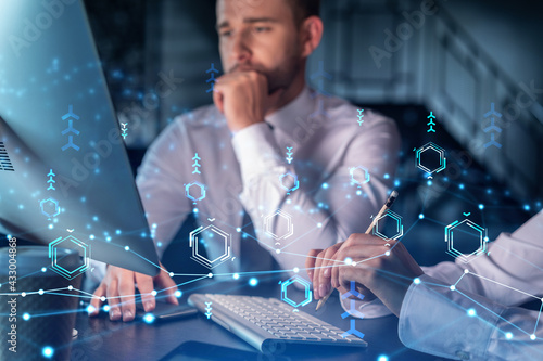 Two colleagues in formal wear working together to optimize business process by applying new technologies. Hi tech holograms over modern office background with panoramic windows photo