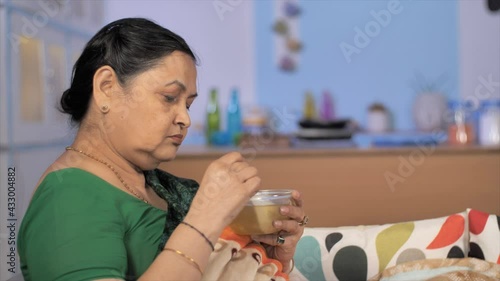 Aged Indian woman having soup / kadha at her home - home treatment for Coronavirus / COVID. Closeup shot of a senior lady drinking her regular liquid diet resting alone indoors - health and nourish... photo