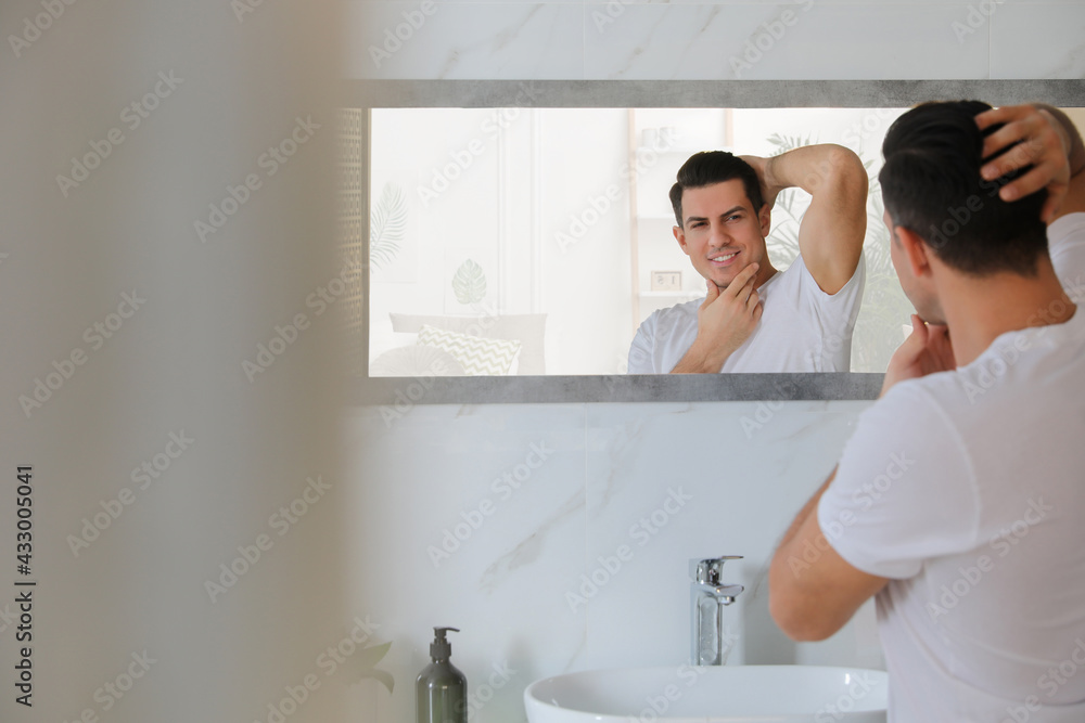 Handsome man touching his smooth face after shaving near mirror in bathroom Handsome man touching his smooth face after shaving near mirror in bathroom