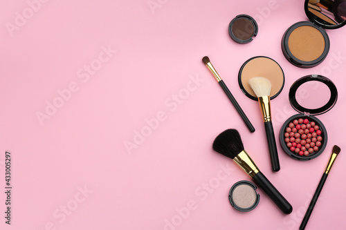 Different makeup brushes and cosmetic products on pink background, flat lay. Space for text