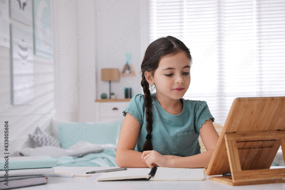 Little girl doing homework with tablet at table in bedroom