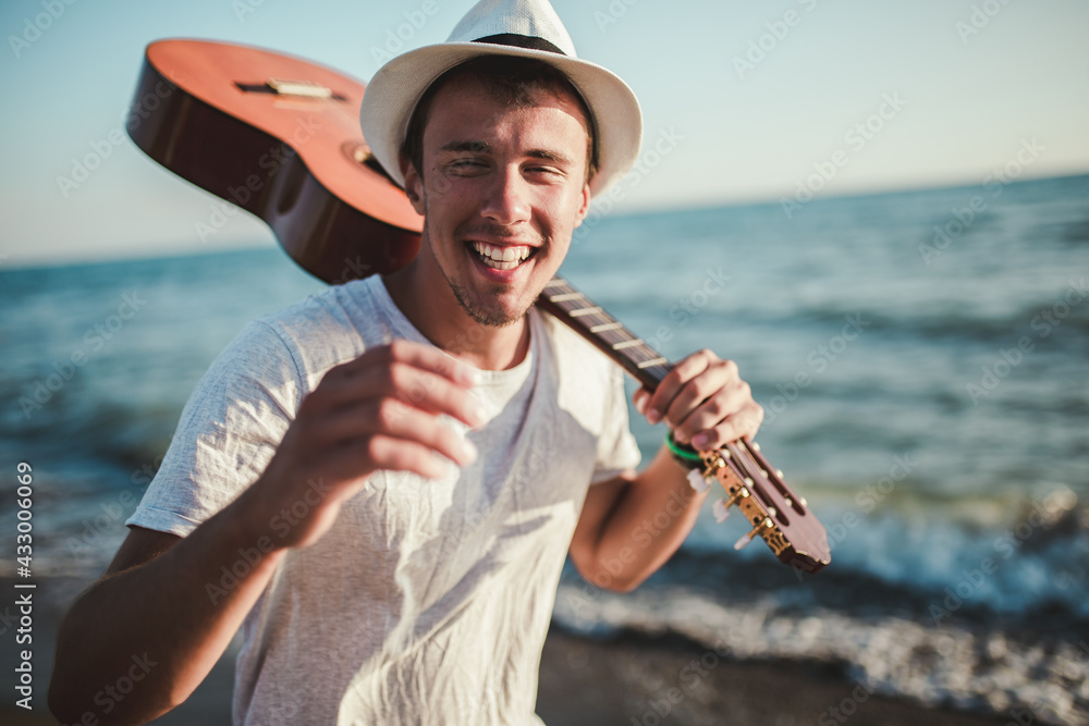 Close up portrait of a young casual man with guitar on his shoulder on the beach