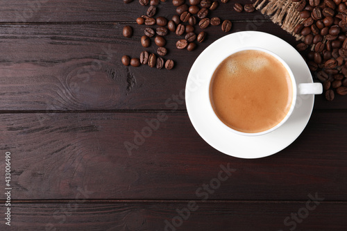 Cup of hot aromatic coffee and roasted beans on wooden table, flat lay. Space for text