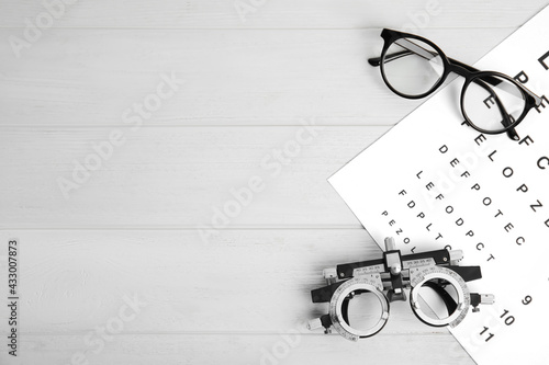 Trial frame, eye chart test, glasses and space for text on white wooden table. Ophthalmologist tools