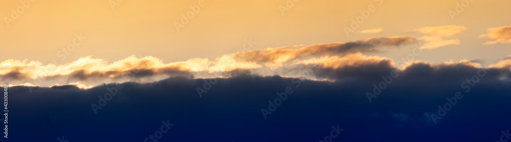 Fototapeta premium Evening sunset panorama with dark blue clouds and orange light clouds.