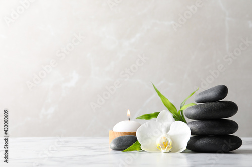 Spa stones, bamboo sprout, burning candle and beautiful orchid flower on white marble table, space for text
