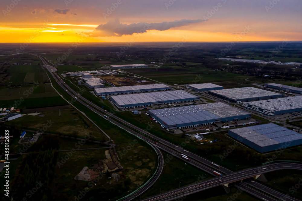 Logistics park with warehouse, loading hub and many semi trucks with cargo trailers standing at the ramps for load and unload goods at sunset.