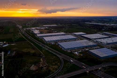Logistics park with warehouse, loading hub and many semi trucks with cargo trailers standing at the ramps for load and unload goods at sunset.