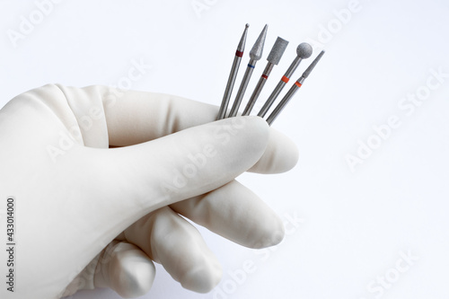 A pedicure specialist in white sterile gloves holds a set of professional diamond cutters for hardware pedicure and manicure on a white background. Space for text. Nail care concept